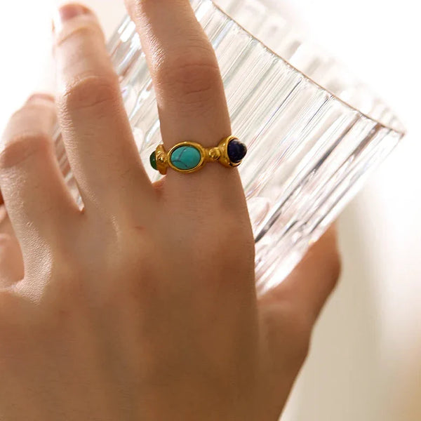 Woman wearing a gold-plated silver ring with blue and turquoise stones, holding a glass