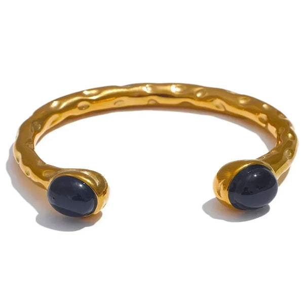 Gold bracelets with colorful stones on a textured surface, branded as Vogue.