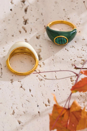 Two rings, one gold and one green, on a textured surface with autumn leaves.