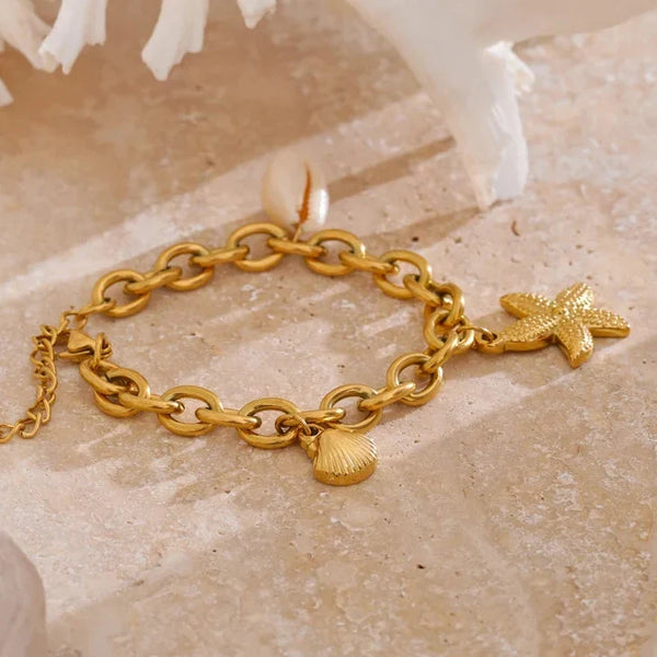 Gold bracelet with starfish and shell charms on a beige stone surface