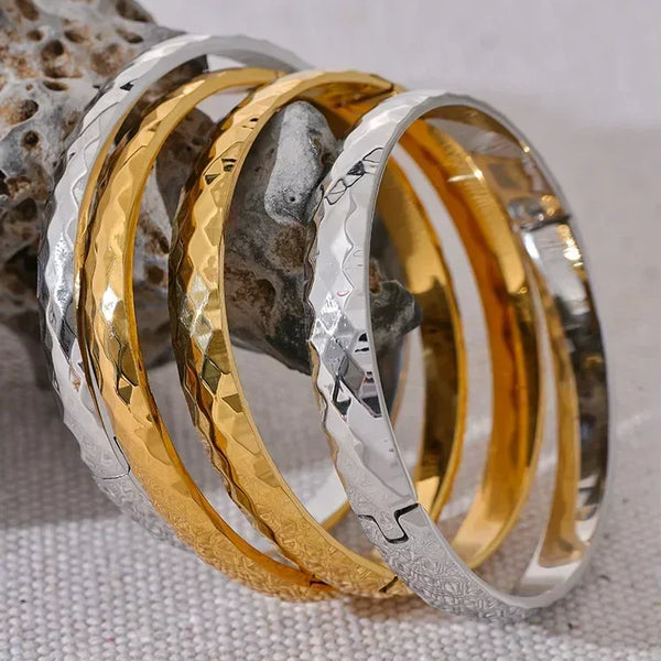 Stacked hammered steel and gold-plated bangles on textured stone, elegant jewelry
