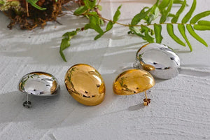 Set of polished 925 silver and 18K gold-plated oval stud earrings on white surface with green leaves