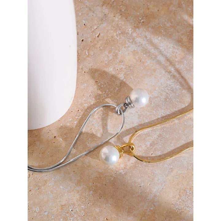 Two pearl necklaces on a beige stone surface