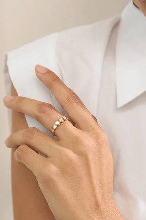 Hand wearing a gold ring with small stones, against a neutral background