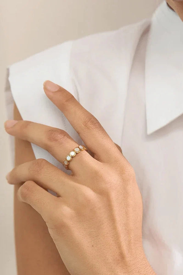 Hand wearing a gold ring with small stones, against a neutral background
