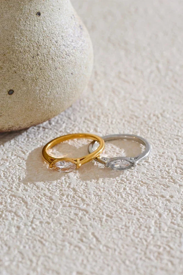 Two rings, one gold and one silver, on a textured surface with a stone in the background.
