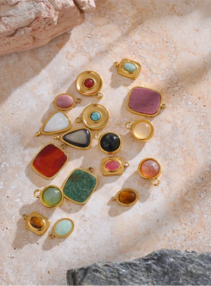 Gold jewelry charms with multicolored stones on a textured stone surface