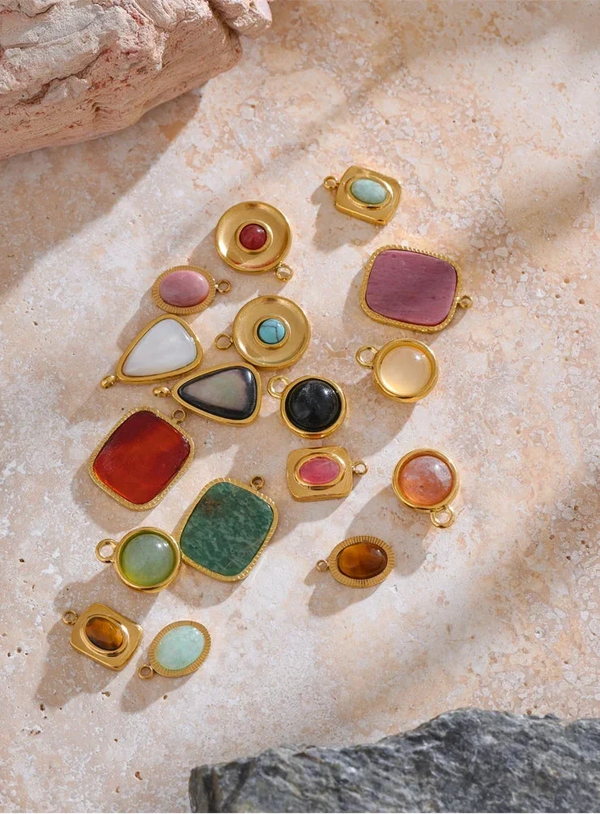 Gold jewelry charms with multicolored stones on a textured stone surface