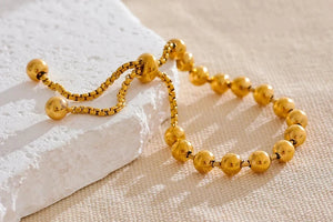 Gold beaded bracelet on a textured white and beige surface