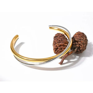 Dual-tone 18K gold-plated and silver cuff bracelet displayed with pine cones on white background