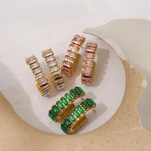 Set of gold hoop earrings with pink and green gemstones on a white and beige stone surface.