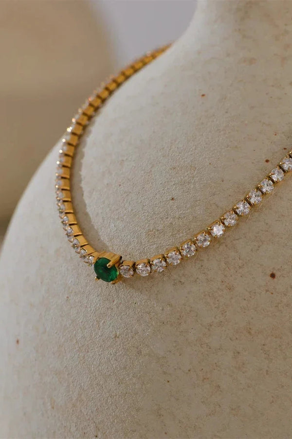 Gold necklace with emerald and diamonds on a beige surface