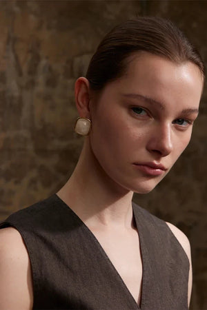 Woman wearing pearl earrings against a textured brown background