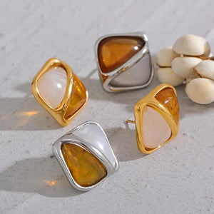 Set of gold and silver earrings on a light gray surface with white flowers.