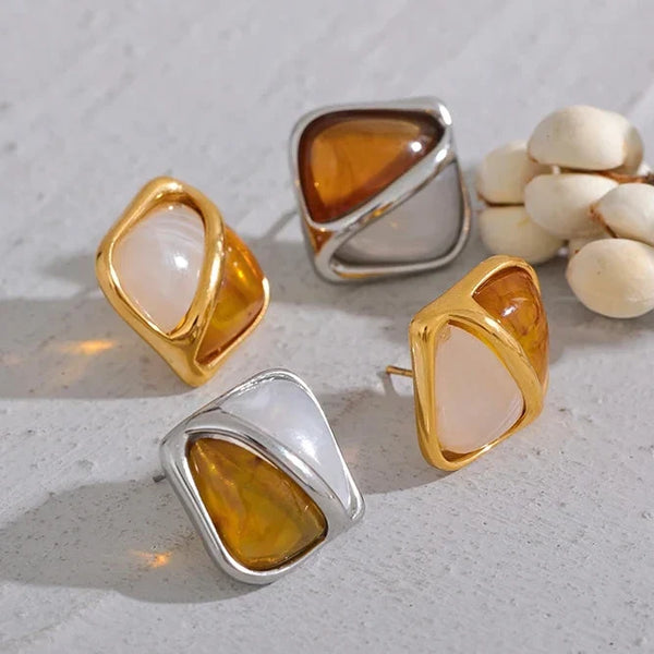 Set of gold and silver earrings on a light gray surface with white flowers.