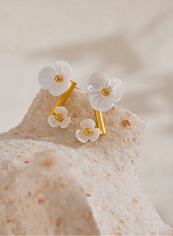 Floral earrings with gold accents on a textured beige surface