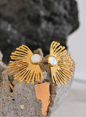 Gold earrings with white stones on a textured surface
