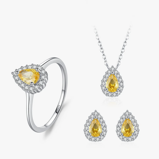 A jewelry set featuring a silver ring, pendant necklace, and matching stud earrings, each with a pear-shaped yellow gemstone surrounded by small clear stones, shown on a clean white background.