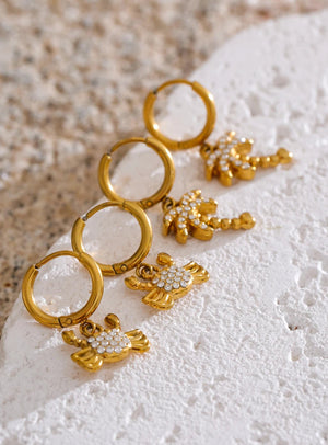 Gold earrings with floral designs on a textured white surface