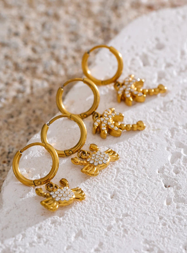 Gold earrings with floral designs on a textured white surface