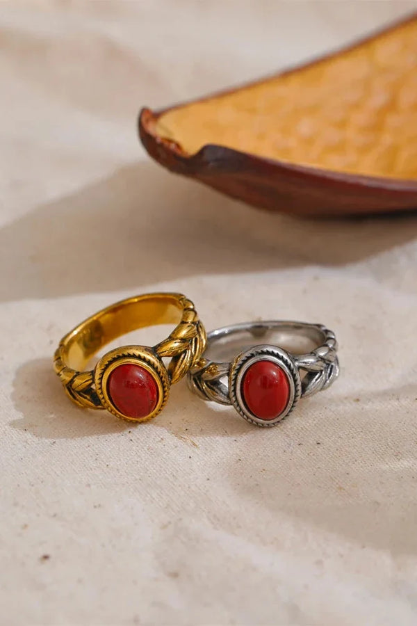 Two rings with red stones, one gold and one silver, on a textured surface.