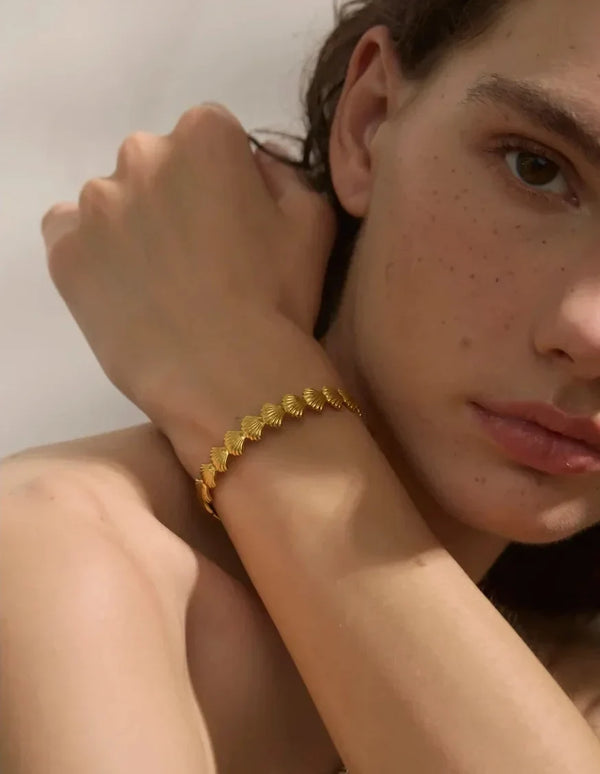 Close-up of a person wearing a gold bracelet on a neutral background
