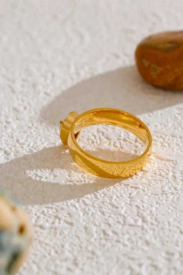 Gold ring on a textured white surface with a stone in the background