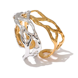 An abstract, open cuff ring featuring a dual-tone metallic design with one textured gold section and one textured silver section, displayed on a clean white background with soft shadows.