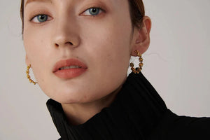 Close-up of a person wearing gold hoop earrings with a neutral background