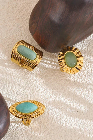 Gold earrings with green stones on a textured surface
