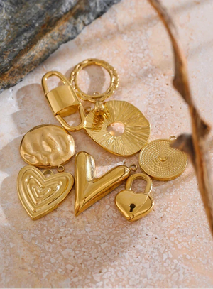 Gold charms including hearts and a lock on a textured stone surface