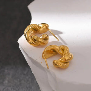 Gold snake-shaped earrings on a white surface with a dark background