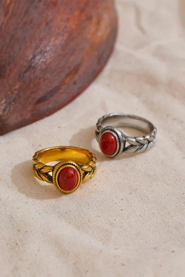 Two rings, one gold and one silver, with red stones on a beige fabric background.