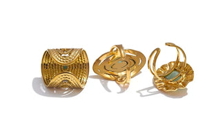 Three views of a gold-toned statement ring on a white background under the  The ring features textured geometric patterns, a spiral openwork center, and a petal-like backplate with a small light blue-green stone.