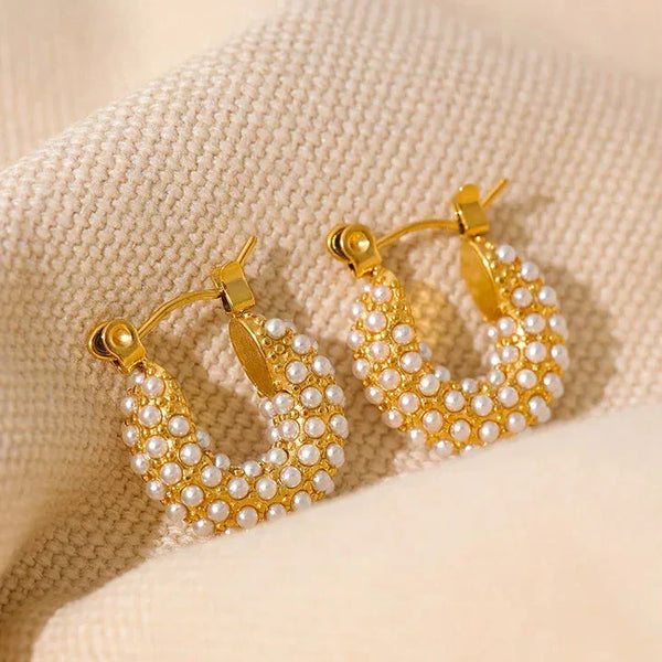 Gold-plated hoop earrings with white pearl accents on a beige fabric background