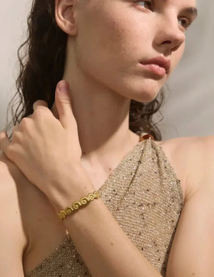 Woman wearing a gold bracelet on her wrist with a neutral background