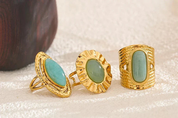 Three gold rings with green gemstones on a textured surface