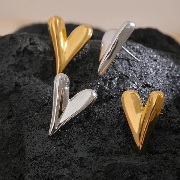 Pair of gold and silver heart-shaped earrings on a dark textured surface.