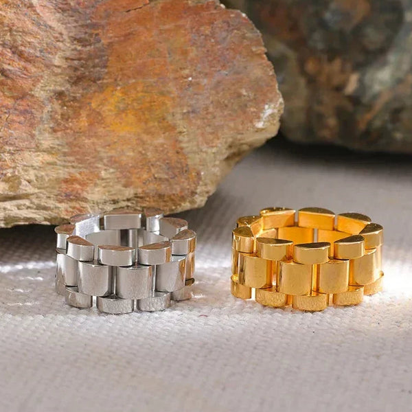 Silver and gold chunky chain rings on textured fabric with natural stone background