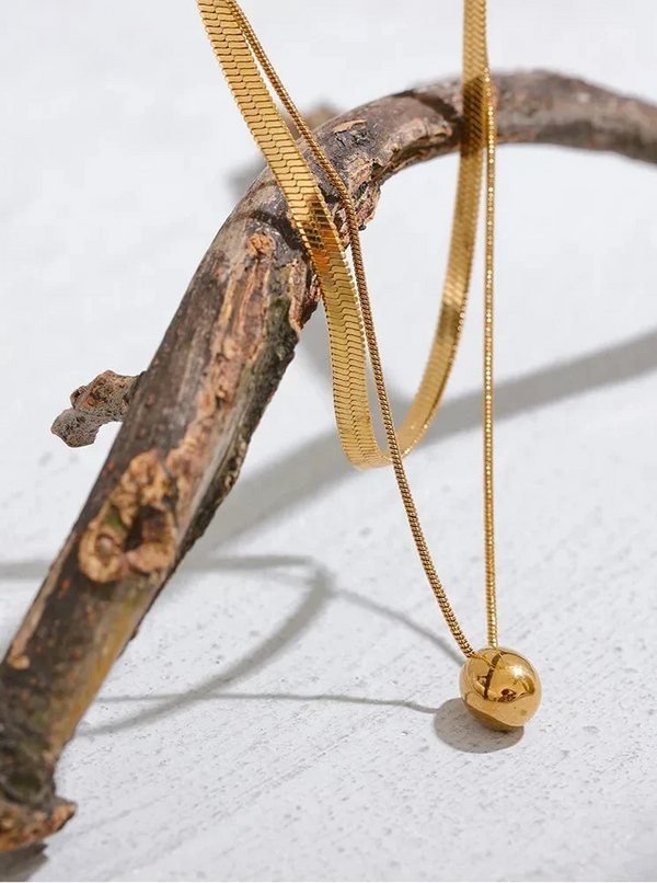Gold necklace with a spherical pendant on a wooden branch