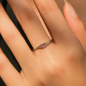 Silver ring with a red gemstone on a person's finger against a neutral background