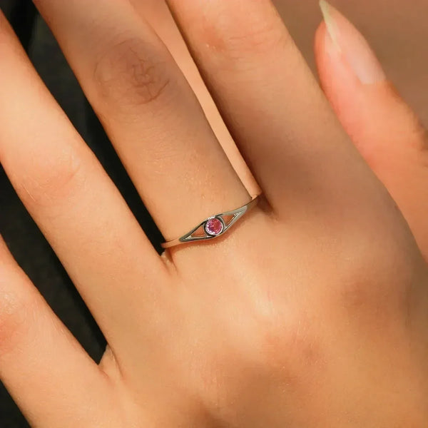 Silver ring with a red gemstone on a person's finger against a neutral background