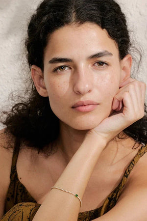 Woman with dark hair and freckles resting her head on her hand against a neutral background
