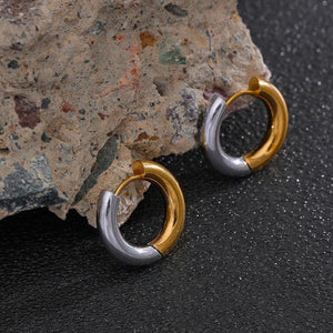 Pair of gold and silver hoop earrings on a textured stone surface with 'Vogue' branding.