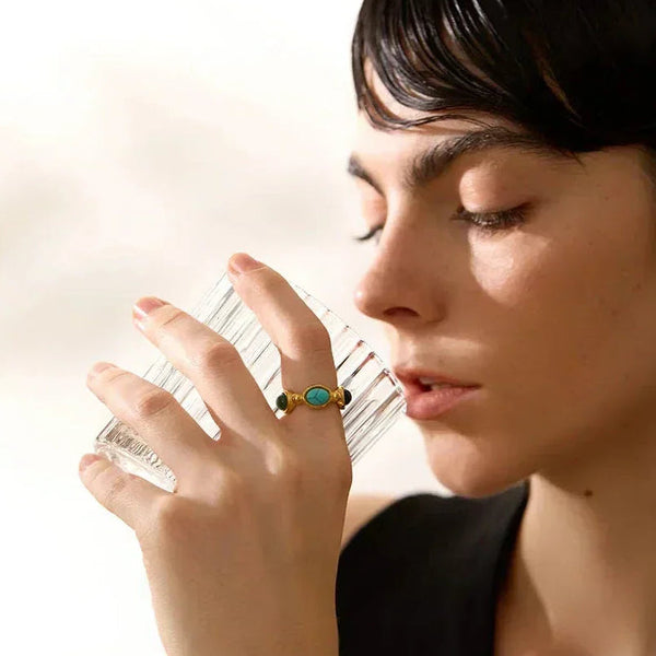 Woman wearing a gold-plated turquoise ring, holding a clear glass, close-up jewelry shot