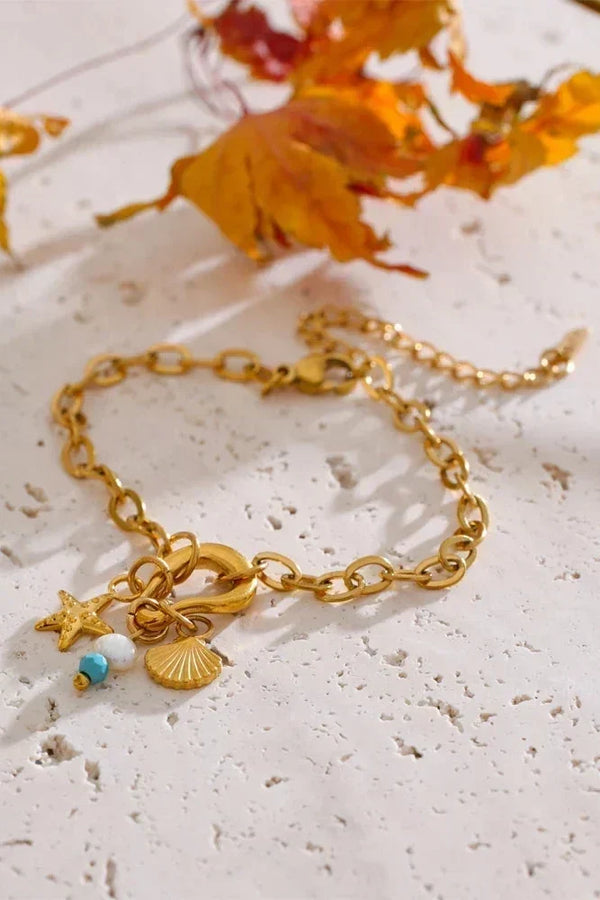 Gold bracelet with charms on a textured surface with autumn leaves