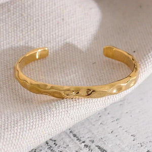 18K gold-plated hammered cuff bracelet on textured fabric background