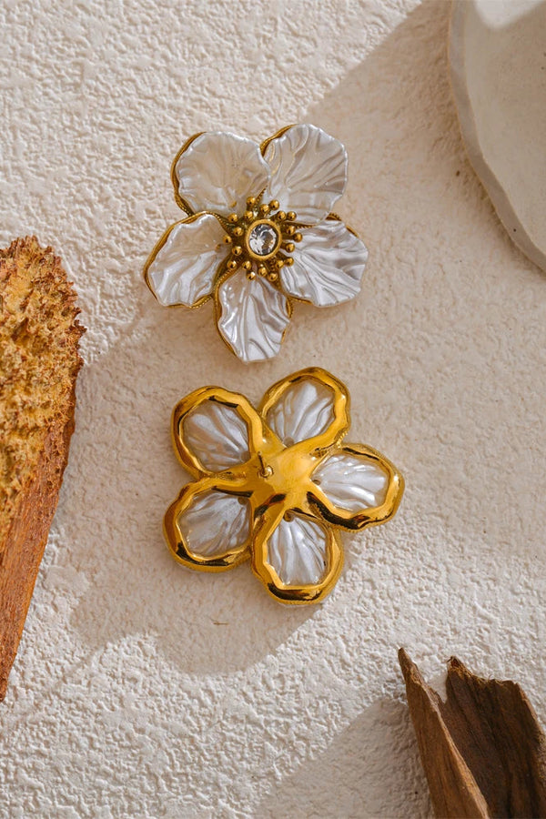 Gold and white floral earrings on a textured surface with natural elements.