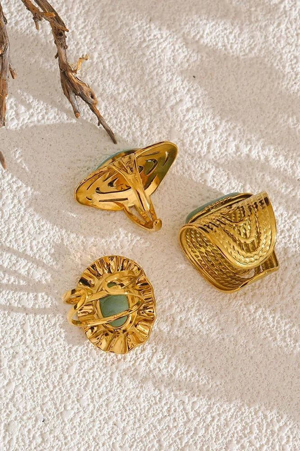Three gold rings with green stones on a textured beige surface
