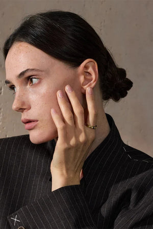Woman in a black pinstripe suit with her hand near her face against a neutral background